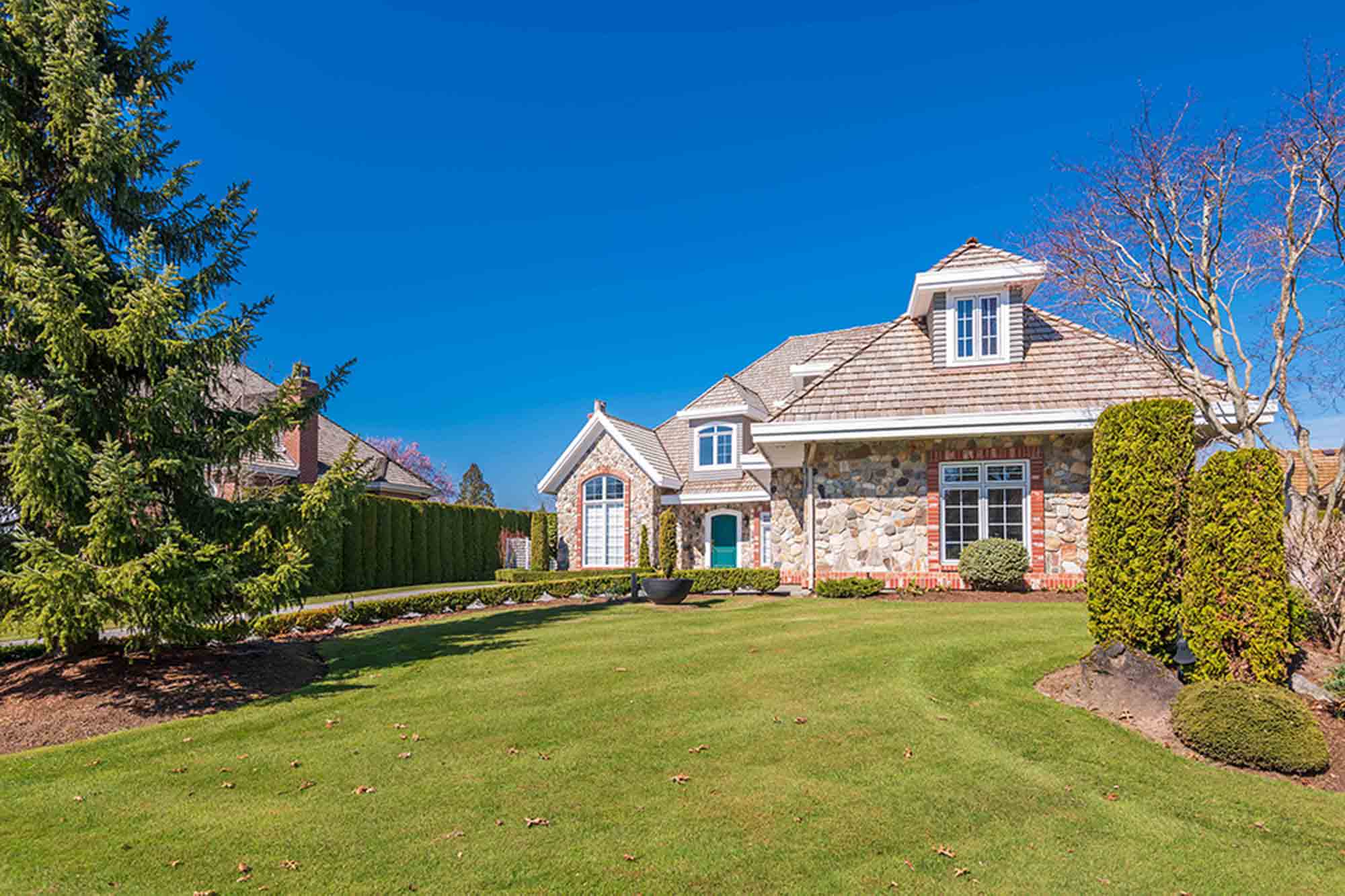Spacious residential front yard with manicured lawn, stone-clad home, ornamental evergreens, and mature trees in Ontario