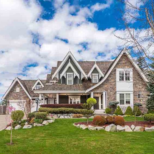 Elegant residential front yard with manicured lawn, stone-clad house, decorative rock beds, and trimmed shrubs in Ontario