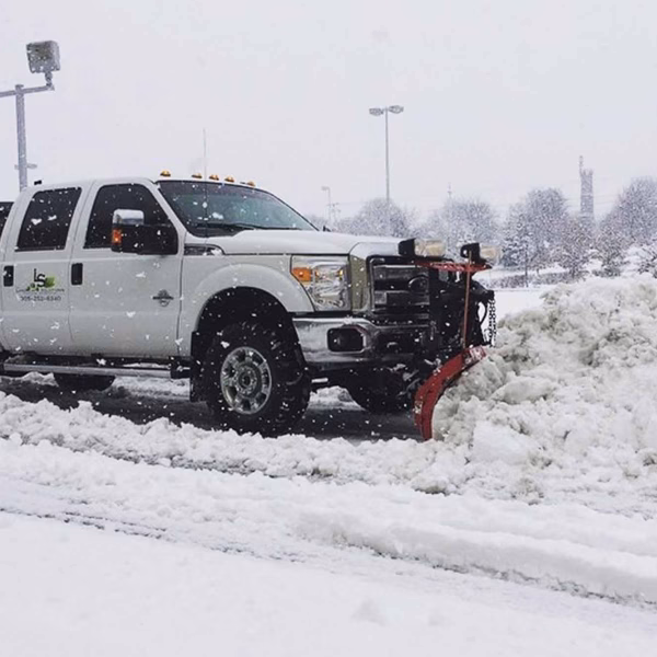 White pickup truck with snowplow clearing a parking lot during heavy snowfall